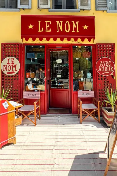 Milan, İtalya - Nisan 07, 2025: Le Nom butiğinin vitrininde kırmızı boyalı giriş, el yapımı çantalar, çizgili sandalyeler ve dekoratif unsurlar. Ön görünüm.