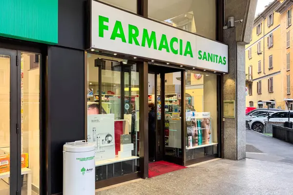 Milan, İtalya - Nisan 07, 2025: Parlak yeşil harfleri ve vitrininde sağlık ürünleri sergilenen modern bir eczane olan Farmacia Sanitas caddesi manzarası.