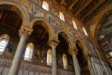 Monreale, İtalya - 25 Temmuz 2024: büyük kemerli katedralin içi, süslemeli sütunlar, dini sahneleri gösteren ayrıntılı mozaikler. Güneş ışığı pencerelerden süzülüyor, altın aksanları aydınlatıyor.