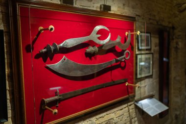 San Gimignano, İtalya - 01.05.2021: Müzede sergilenen tarihi silahların koleksiyonu, kırmızı arka planda çeşitli ortaçağ bıçaklarının yer aldığı