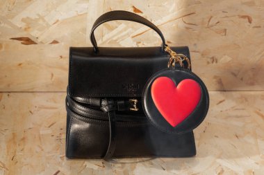 Milan, İtalya - 12 Nisan 2025: kırmızı kalp tılsımlı siyah Moschino marka mini çanta. Ahşap arkaplan görüntüsünde tasarımcı aksesuarı.
