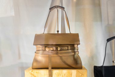 Milan, İtalya - 12 Nisan 2025: Moschino taupe kahverengi deri çantalı ve vitrininde kemer ayrıntıları olan çanta. Minimalist şık, ön manzara.