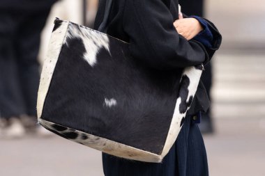 Paris, Fransa - 11 Mart 2025: Kadın kolunun altına büyük siyah beyaz bir sığır derisi çanta takıyor. Koyu derili, doğal deri desenli. Eşsiz hayvan desenli aksesuar.