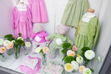 Milan, İtalya - 09 Nisan 2025: Çocuk moda gösterisi. Pembe ve yeşil gingham elbiseler, oyuncak ayılar ve bahar çiçekleri mağazanın vitrininde.