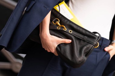 Paris, Fransa - 11 Mart 2025: Kadın siyah Miu Miu marka çanta takıyor, altın tokalı donanım ve sarı zarf ile donanma ceketinin altına takılıyor. Sokak tarzı kıyafet ayrıntıları.