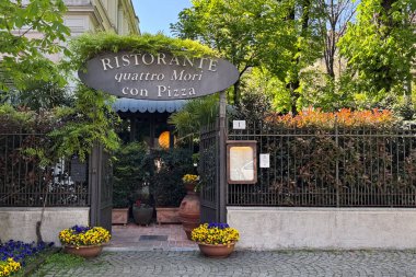 Milan, İtalya - 11 Nisan 2025: Quattro Mori restoran girişi eski tabelası ve yemyeşil bahçesi ile. Geleneksel İtalyan pizzacısı. Bahar sahnesi.