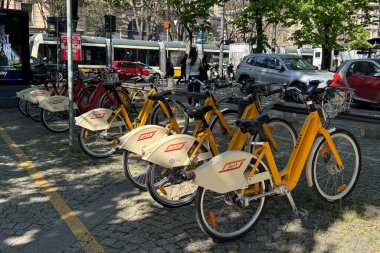 Milan, İtalya - 11 Nisan 2025: Ağaçların altına park edilmiş sarı bisikletli bisiklet istasyonu. Kamu bisiklet paylaşım sistemi. Şehir ulaşımı.