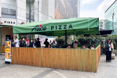 Milan, İtalya - 12 Nisan 2025 Alice Pizza yeşil paraşütü ve teras dolusu restoran. İnsanlar popüler pizzacının önünde kuyruğa giriyor. Milan şehir merkezinde yoğun bir gün..