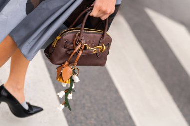 Paris, Fransa - 11 Mart 2025: Küçük kahverengi deri deri Miu Miu el çantası ve çiçekli anahtarlık. Sokak tarzı kıyafet ayrıntıları.