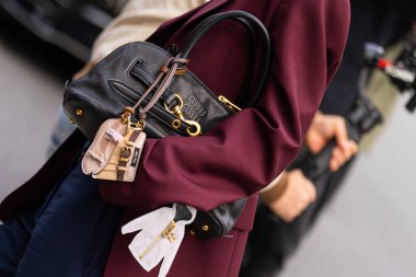 Paris, Fransa - 11 Mart 2025: Kadın altın aksanlı siyah deri Miu Miu çanta giyiyor ve anahtarlık takıyor. Bordo ceketin altına giyilmiş. Sokak tarzı kıyafet ayrıntıları.