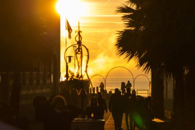 Sirmione, İtalya - 01.01.2022: Siluetli insanlar ve palmiye ağaçları, Garda Gölü 'nde sakin gün batımı.