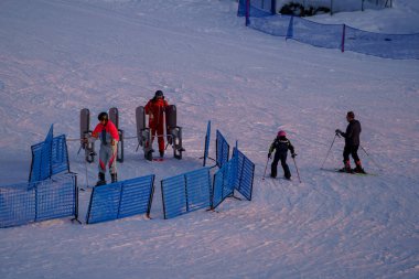 Piani di Bobbio, İtalya - 24.12.2022: Kayakçılar yollarına mavi güvenlik bariyerleriyle karlı yamaçta asansör kapısına yaklaşıyorlar. Kış boyunca kayak merkezindeki organizasyon ve faaliyetler