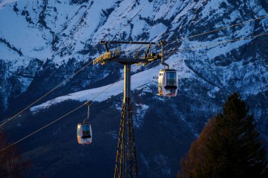 Piani di Bobbio, İtalya - 24.12.2022: Kablolu arabalar destek kulesinin yanından geçiyor. Kışın kayak merkezinde kayak yapan insanlar. Tatiller, kar giysileri kiralama, kayak, snowboard ve dağ manzarası konsepti