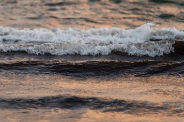 Alacakaranlıkta denizin yüzeyinde yuvarlanan yumuşak dalgaların yakın çekimi. Yumuşak ışık sudan yansıyarak huzurlu ve huzurlu bir atmosfer yaratır.