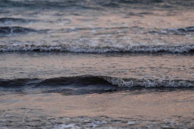 Alacakaranlıkta denizin yüzeyinde yuvarlanan yumuşak dalgaların yakın çekimi. Yumuşak ışık sudan yansıyarak huzurlu ve huzurlu bir atmosfer yaratır.