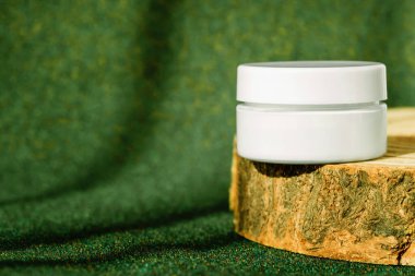 Kolajenle sıkılaştırılmış krem kavanozu yeşil toprak tonlu arka planda ahşap ekrana yerleştirilmiş. Creme modelleme, podyumda marka ambalajlama, cilt ürünleri, güneş kremi modelleme