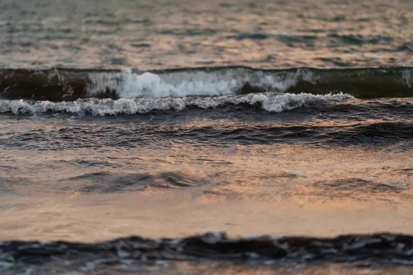 Alacakaranlıkta denizin yüzeyinde yuvarlanan yumuşak dalgaların yakın çekimi. Yumuşak ışık sudan yansıyarak huzurlu ve huzurlu bir atmosfer yaratır.