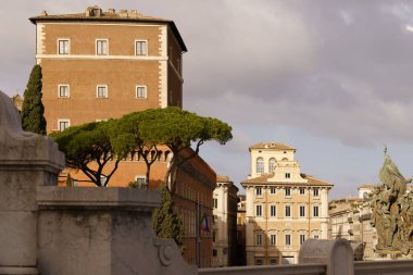 Roma, İtalya - 09.12.2022: Yüksek selvi ağaçları ve bulutlu gökyüzü ile tarihi İtalyan mimarisi Palazzo Venezia.