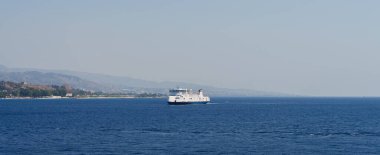 Sicilya, İtalya - 27.07.2024: Sahil dağları yakınlarındaki sakin sularda feribot ile sakin deniz manzarası.
