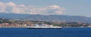 Sicilya, İtalya - 27.07.2024: Mavi sular ve dağlık ufuk arasında feribot bulunan manzaralı kıyı manzarası.