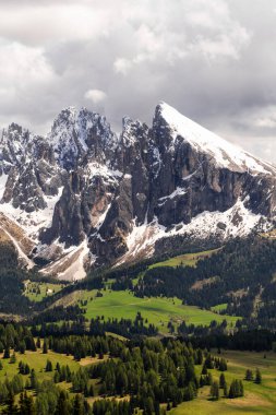 İtalya 'nın Dolomites kentindeki Funes Vadisi yakınlarında, dramatik gökyüzü altında karla kaplı tepeleri ve yemyeşil vadisi olan görkemli dağ sıraları..