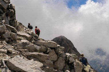 Passo Tonale, İtalya - 10.08.2024: Maceracılar heybetli manzarada bulutlu gökyüzü ile kayalık dağ patikasına tırmanıyorlar.