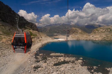 Passo Tonale, İtalya - 10.08.2024: Alp gölü ve kayalık arazi üzerinde manzaralı dağ teleferiği yolculuğu.