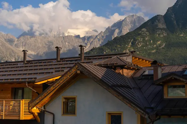 Passo Tonale, İtalya - 10.08.2024: Gün batımında bulutlu gökyüzünün altında manzaralı Alp arka planlı dağ evi.