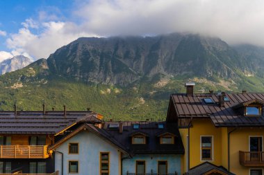 Passo Tonale, İtalya - 10.08.2024: Yeşillik ortasındaki büyüleyici köy evleri ile manzaralı dağ manzarası.