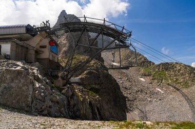 Passo Tonale, İtalya - 10.08.2024: Kayalık arazisi ve yazın engebeli zirveleri olan dağ teleferiği istasyonu.
