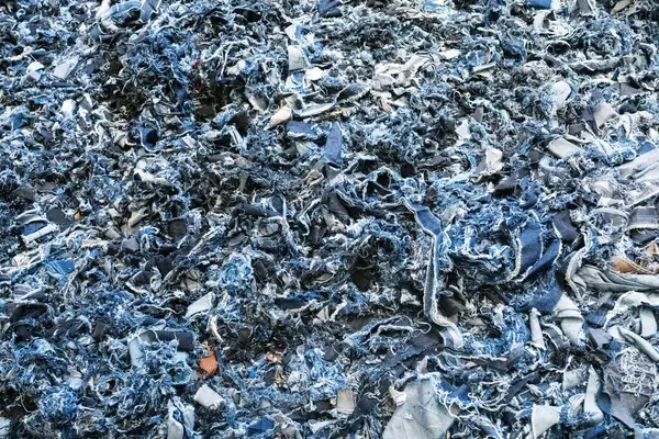 Paramparça kot kumaş kırıntıları. Sürdürülebilir moda üretiminde veya çevre dostu tekstil ürünlerinde yeniden kullanılmak üzere geri dönüştürülmüş eski mavi tekstil parçaları. Çiğ doku, makro çekim. Geri dönüştürülmüş kot