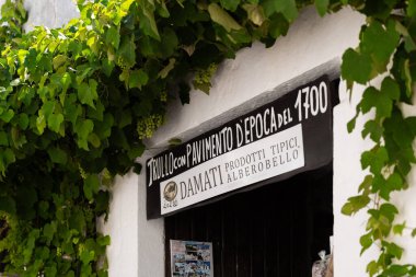 Alberobello, İtalya - 30.07.2023: İtalya 'nın Alberobello kentindeki geleneksel mağazanın girişinde yeşil üzüm kümeleriyle dolu yemyeşil bir dedikodu yetişiyor. Dükkan girişini imzala