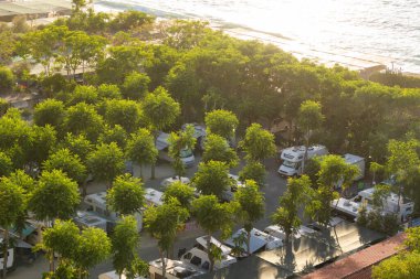 Tropea, İtalya - 27.07.2023: Sahile yakın yemyeşil ağaçların altında parkedilmiş karavan karavanları olan sahil kamp alanı.