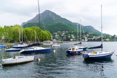 Lecco, İtalya - 01.05.2023: Sahil tekneleri, İtalya 'nın Como Gölü yakınlarındaki yemyeşil yemyeşil ve tepe kenarındaki evlerle çevrili sakin dağ gölüne huzurlu bir şekilde kenetlendi