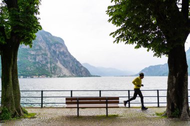 Lecco, İtalya - 01.05.2023: Lungolago di Lecco, İtalya 'da hızlı koşan adam. Sağlıklı yaşam tarzı, spor koşucusu göl kenarında yaz parkı işletiyor Como