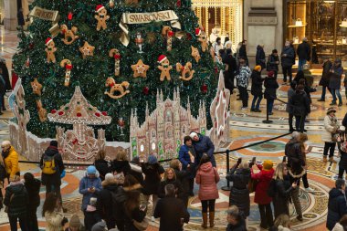 Milan, İtalya - 18.12.2022: Noel ağacı etrafında zencefilli ekmek adamlar ve festival ışıklarıyla süslenmiş büyük bir kalabalık toplandı. İnsanlar Victor Emmanuel 'in galerisinde fotoğraf çekiyor ve tatil ruhunun tadını çıkarıyor.