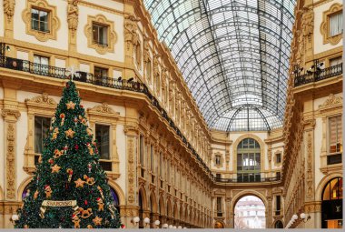Milan, İtalya - 18.12.2022: Victor Emmanuel 'in süslü tarihi bir alışveriş galerisinde şenlikli süslemelerle süslenmiş büyük bir Noel ağacı. Lüks tatil ortamı