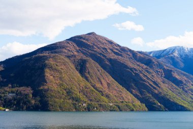 Tepelerin eteklerine yerleşmiş dağ ve Como Gölü 'nün geniş panoramik manzarası. Dağınık bulutlu açık mavi gökyüzü İtalya 'nın huzurlu ve manzaralı atmosferine ekleniyor
