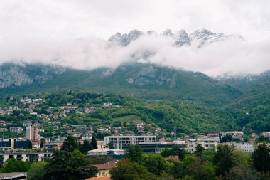 Lecco, İtalya - 19.05.2024: Bereketli yeşillik ve bulutlarla kaplı zirveleri olan manzaralı dağ ve kasaba manzarası.