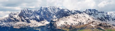 İtalya 'nın Dolomites kentindeki Funes Vadisi yakınlarındaki bulutlu gökyüzü manzarasının altındaki görkemli kar örtülü sıradağlar..