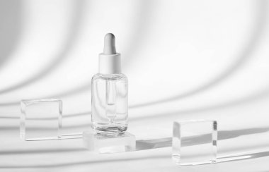 berrak serum şişesi kristal bloklarla çevrili beyaz arka planda zarif gölgeler bırakarak