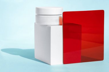 Beyaz kozmetik kavanozu beyaz blokta kırmızı ve mavi akrilik çarşaflarla