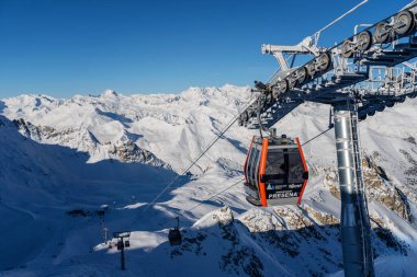 Ponte di Legno, İtalya - 03.12.2023: Parlak kış gününde kablo yayla kaplı dağ zirveleri üzerinde süzülür. Asansörün yapısı buzla kaplıdır ve açık gökyüzü alp manzarasını geliştirir.