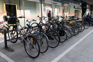 Milan, İtalya - 08 Nisan 2025: kaldırıma park edilmiş bisiklet sıraları. Bisiklet rafı ve mağaza vitrinli şehir sokak sahnesi.