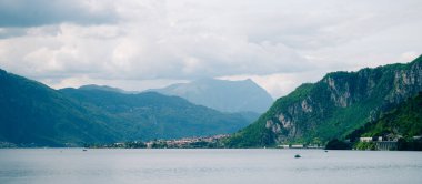 Göl manzarası bulutlu gökyüzünün altında dağlarla ve köyle çevrili.