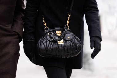Milan, İtalya - 10 Ocak 2024: Kadın altın aksanlı siyah Miu Miu çanta giyiyor. Moda kıyafetleri, sokak tarzı.
