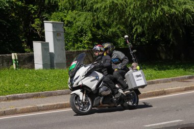 Lecco, İtalya - 29.05.2025: Giro dItalia yarışı sırasında iki etkinlik gazetecisi ile birlikte yol boyunca hareket eden motosiklet. Giro dItalia, her yıl düzenlenen çok aşamalı bisiklet yarışı.