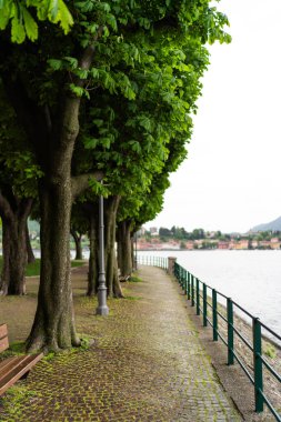 Göldeki patika boyunca uzanan büyük ağaçların gölgesinde sakin bir bank uzanır. İtalya 'nın Como gölündeki Lecco gölünün kıyısındaki uzak köy ve dağların huzurlu manzarasını sunar.