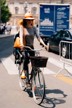 Milan, İtalya - 25 Mayıs 2024: Siyah sepetli bisiklet süren şık bir kadın. Yaz modası, yavaş seyahat ve şehir dışı yaşam tarzı konsepti..