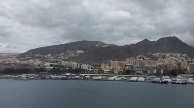 İspanya Santa Cruz de Tenerife 22 Nisan 2024 bereketli dağlara ve bulutlu gökyüzüne karşı kurulmuş pitoresk bir sahil şehri, canlı binalar ve liman hayatı ile kentsel ve doğal uyumu gözler önüne seriyor..
